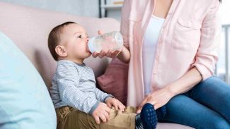 Baby sitzt trinkend auf Sofa was eine Gefahr für Erbrochenes auf dem Sofa darstellt