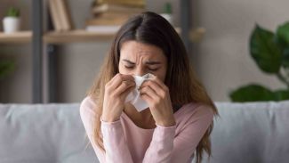 Frau mit Allergie gegen Hausstaubmilben sitzt auf Sofa