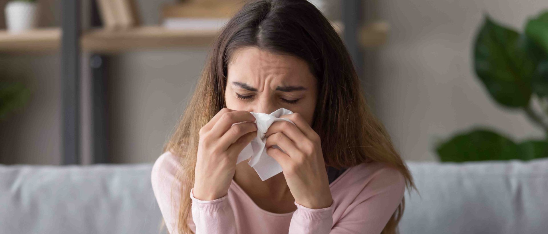 Frau mit Allergie gegen Hausstaubmilben sitzt auf Sofa